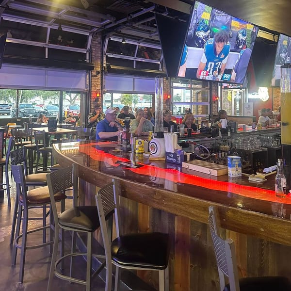 Patrons at the Texas Huddle bar with a large TV screen showing a football game.
