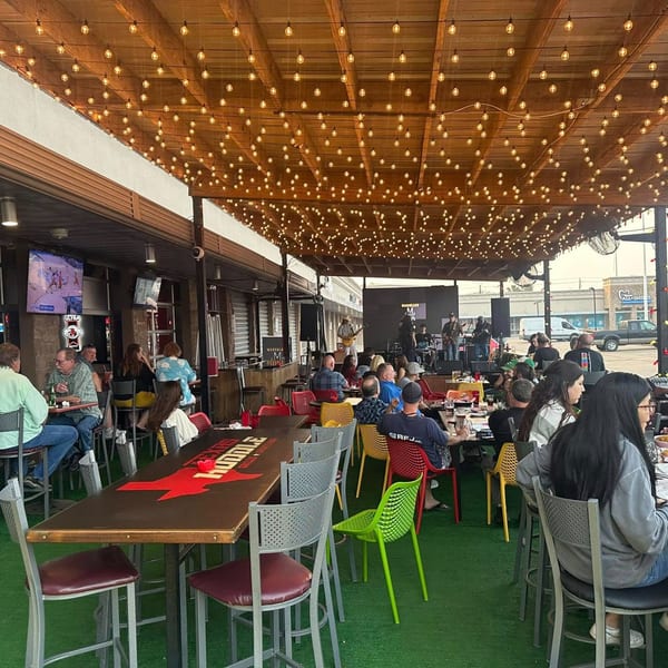 Patrons enjoying live music and drinks on the outdoor patio of Texas Huddle restaurant.